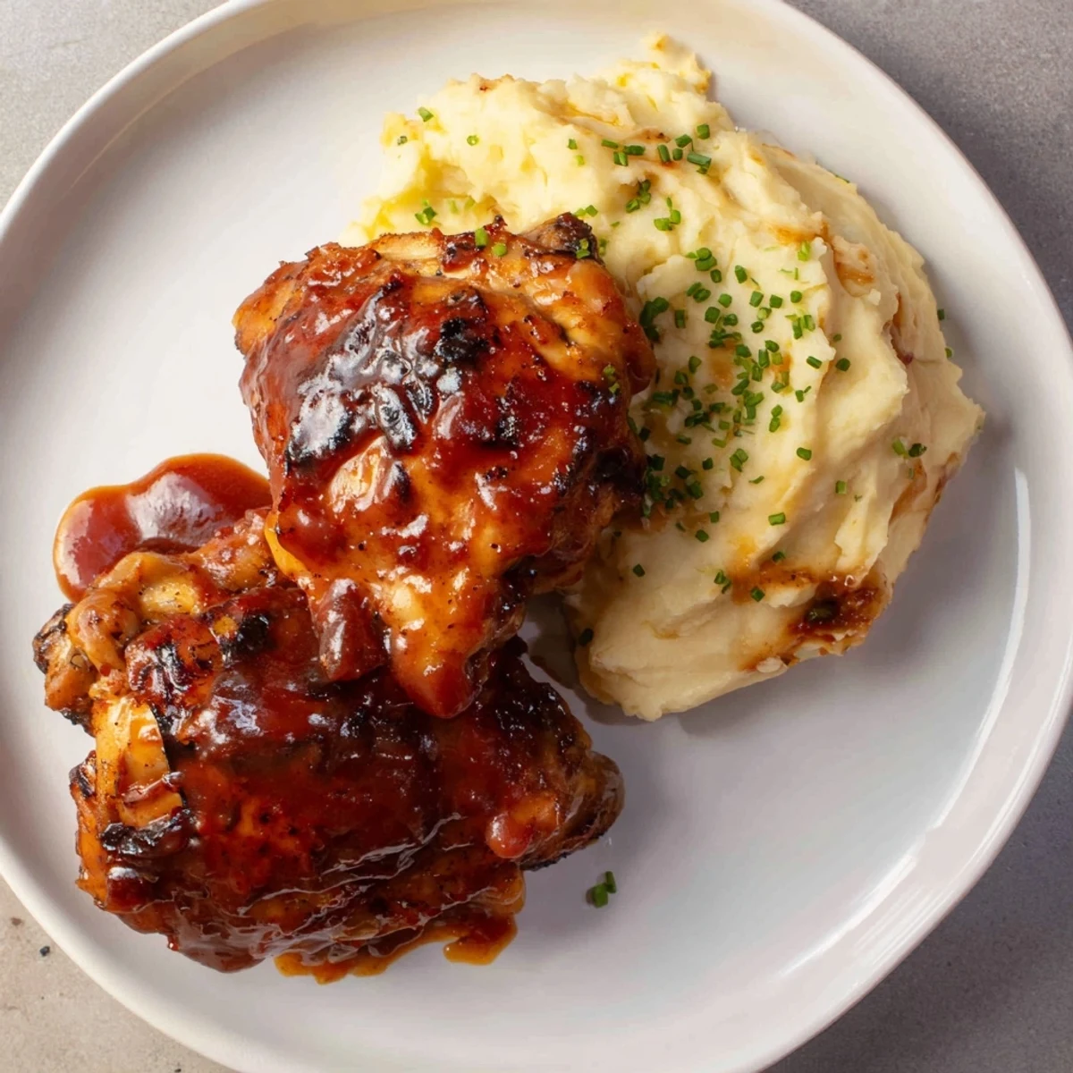 Golden-brown Honey BBQ Chicken Thighs glistening with sauce, served beside fluffy garlic mashed potatoes.