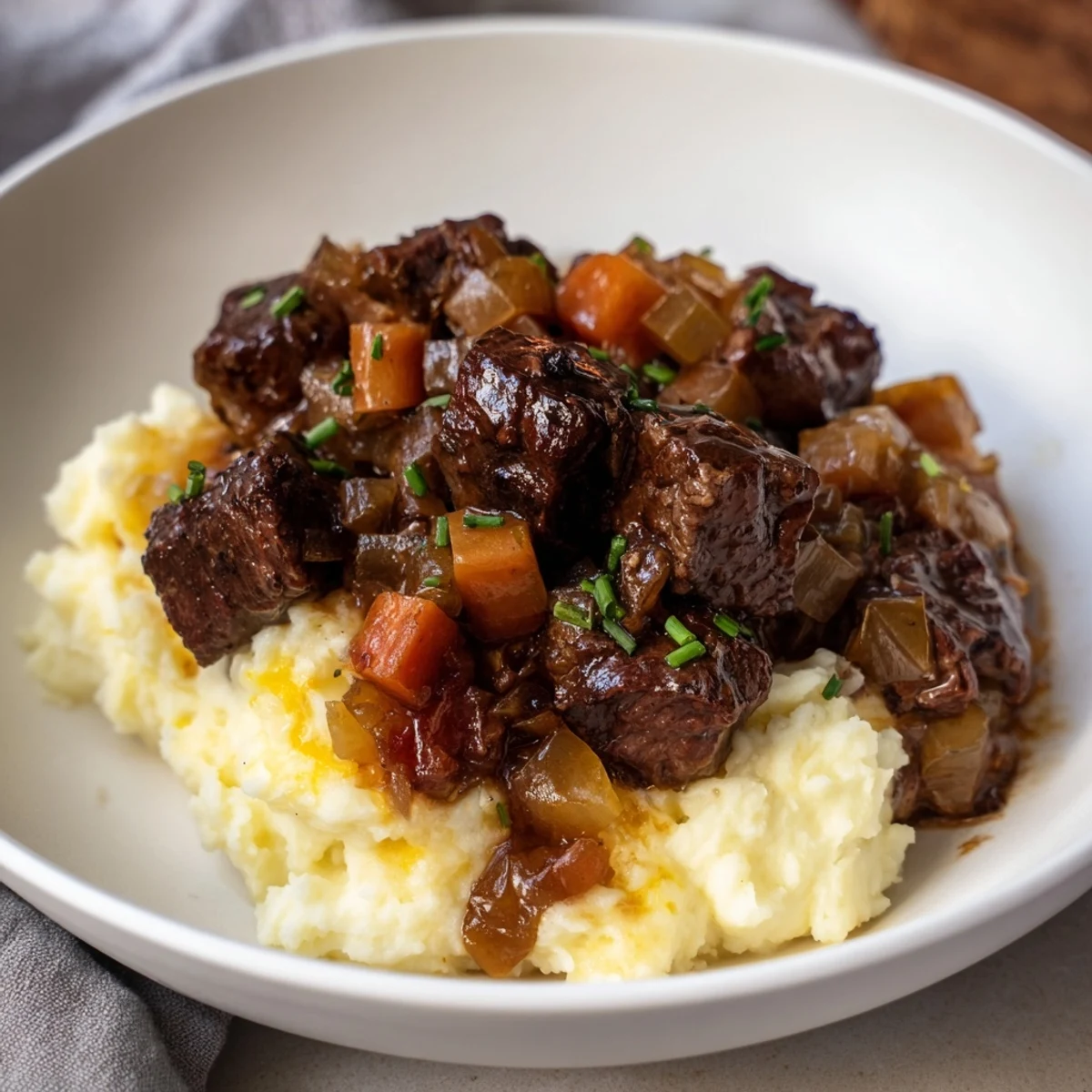 Savory Fall Apple Cider Stew rest on creamy mashed potatoes, sprinkled with fresh chives.