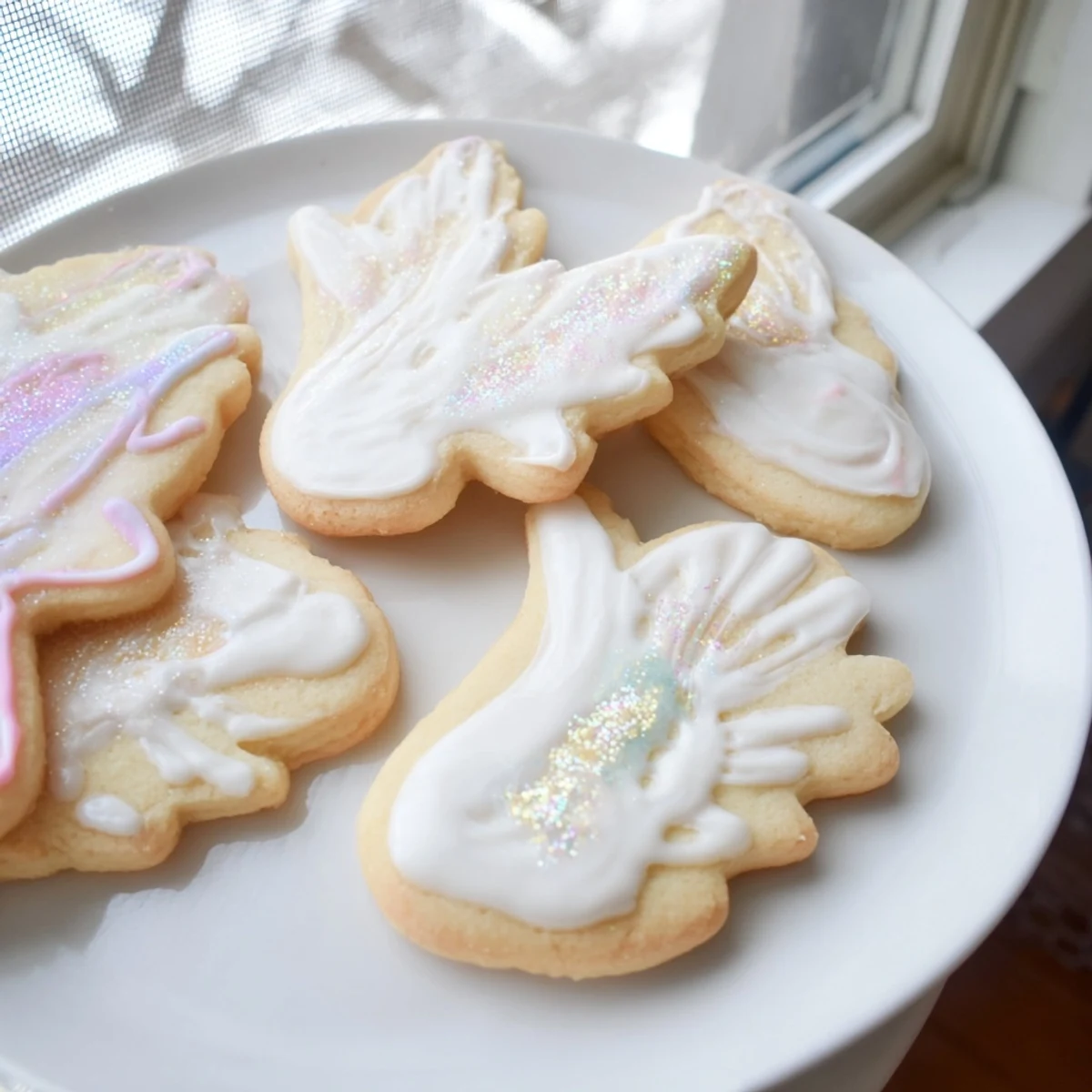 Golden, delicate Angel Wings Sugar Cookies arranged on a plate with shimmering sprinkles, ready to enjoy.