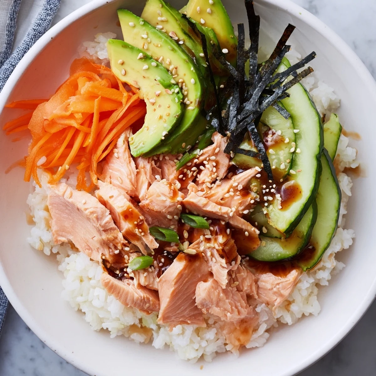 Freshly assembled Japanese-Style Salmon & Chicken Rice Bowl served with avocado and a flavorful sauce.