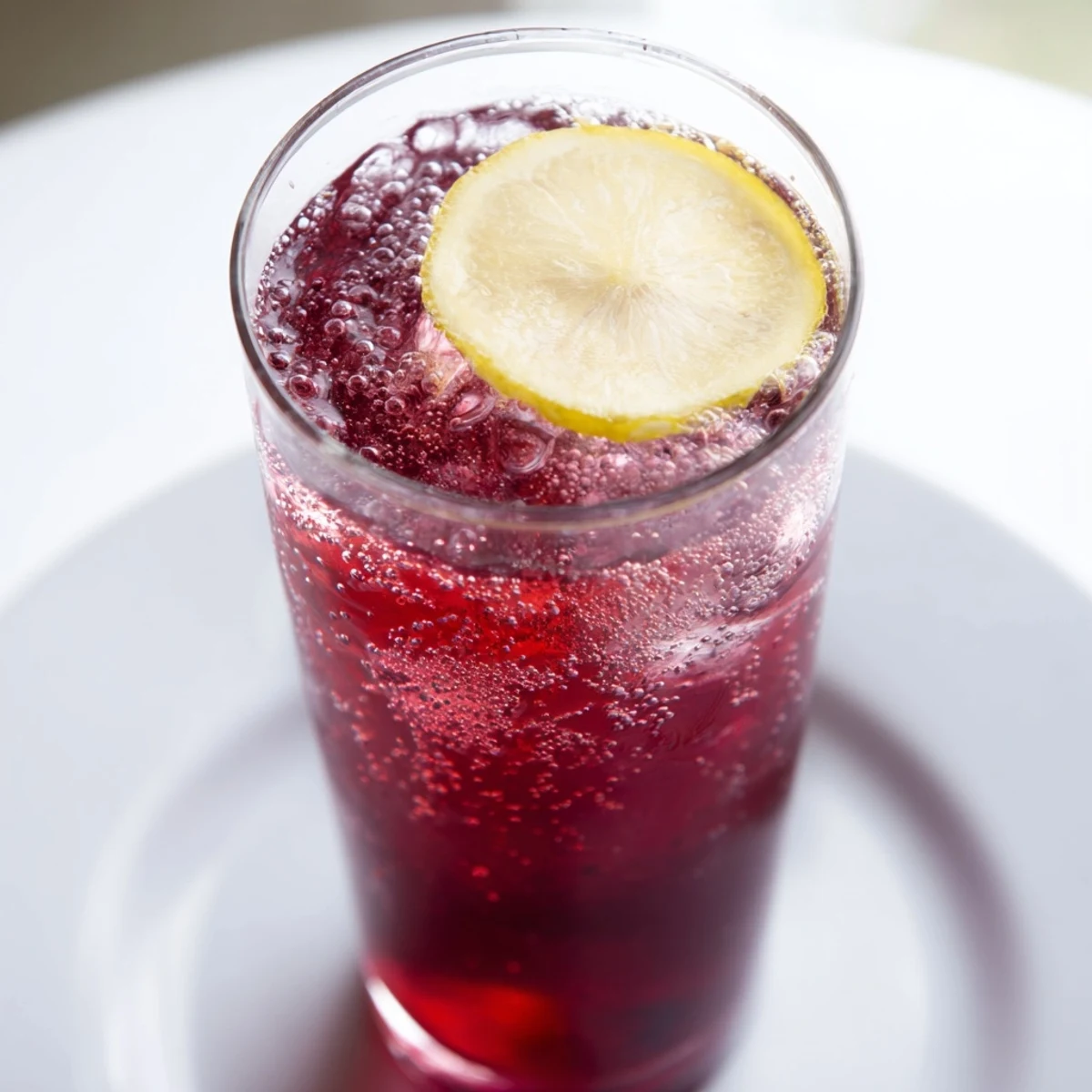 Cool glass holding a deep red Sleepy Girl Mocktail, a refreshing, lightly effervescent bedtime drink.