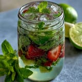 Refreshing virgin mojito pitcher with fresh mint, lime, and strawberries, served in a clear glass pitcher with ice and citrus slices.