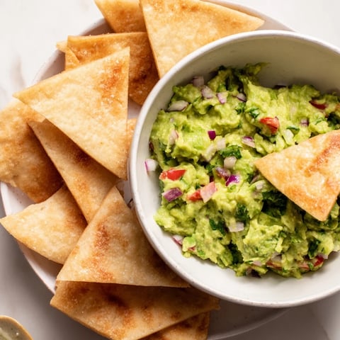 Golden, crispy pita chips surround a vibrant guacamole bowl, a perfect party appetizer.