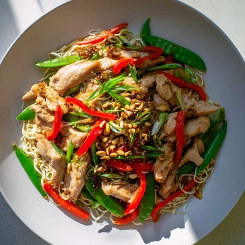 A steaming bowl of Mongolian Chicken with its savory sauce ladled over delicate rice noodles.