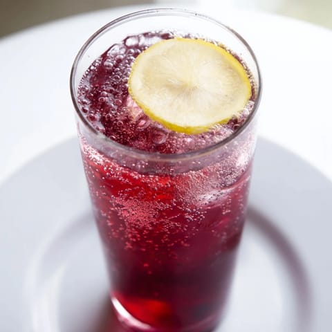 Cool glass holding a deep red Sleepy Girl Mocktail, a refreshing, lightly effervescent bedtime drink.