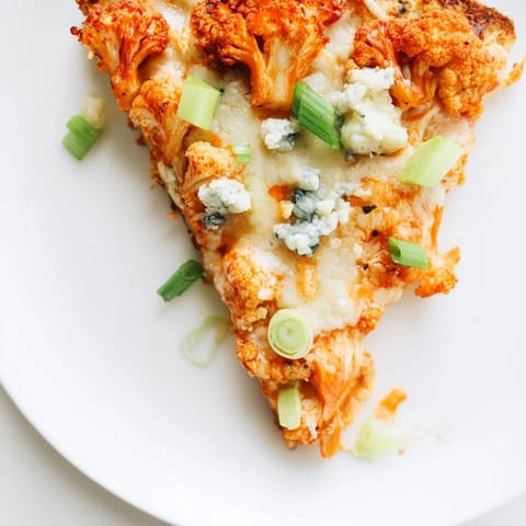 Close-up of a spicy Buffalo Cauliflower Pizza slice topped with crumbled blue cheese and fresh parsley, ready to serve.  