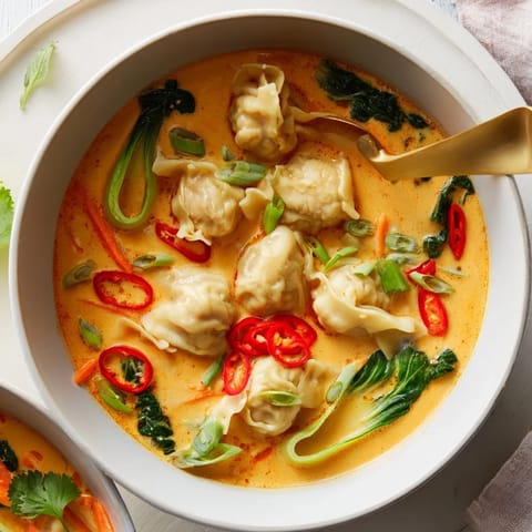 Steaming bowl of Red Curry Wonton Soup with greens, ginger, and cilantro garnish.  