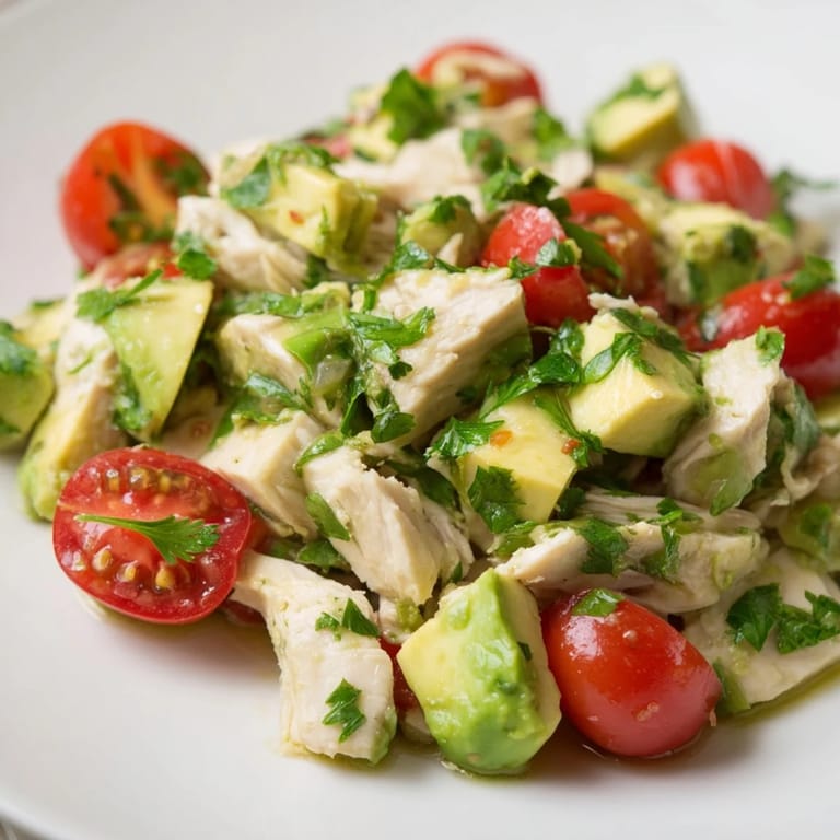 Chilled avocado chicken salad featuring tender diced chicken, ripe avocado chunks, and vibrant cherry tomatoes on a rustic wooden table.