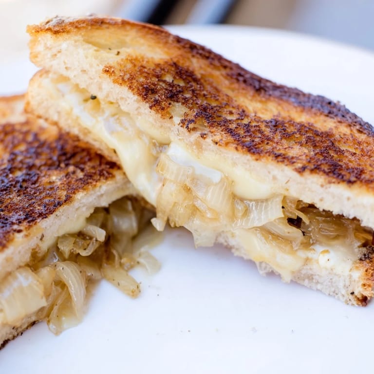 A close-up view of a buttery, golden-brown grilled cheese sandwich filled with nutty Gruyère and deeply caramelized yellow onions.