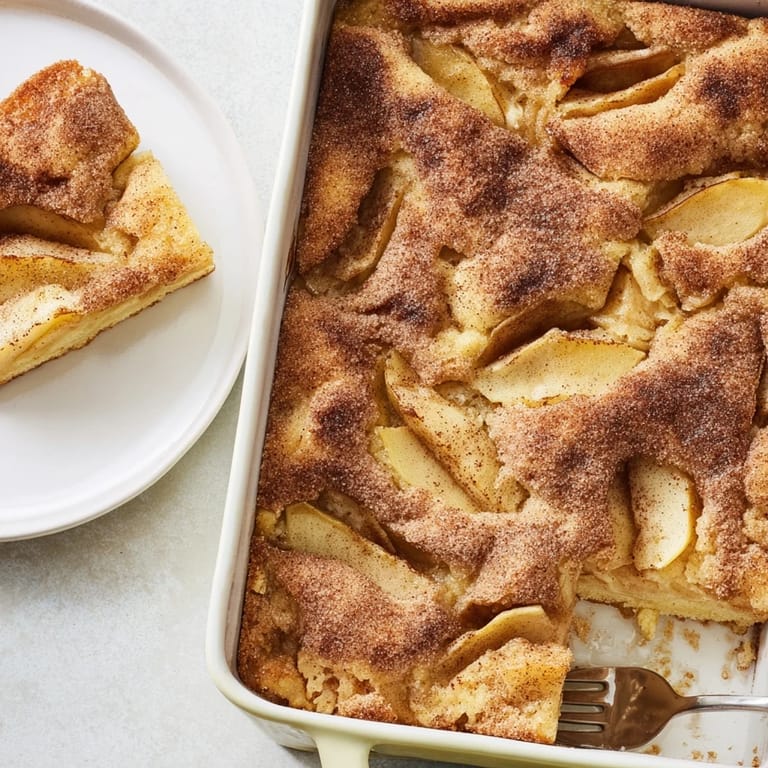 Golden, casserole-style Baked Apple Cake served warm from the oven, dusted with powdered sugar for a cozy breakfast treat.